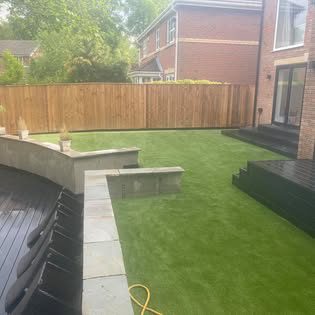 Full garden transformation with raised stone beds, paving and new artificial lawn beside a house extension